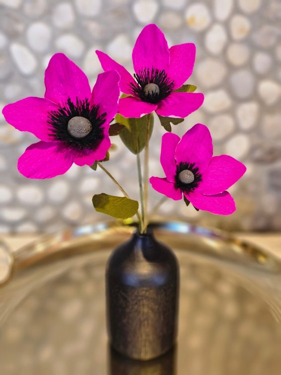 Roze papieren anemonen in een klein bronzen vaasje.