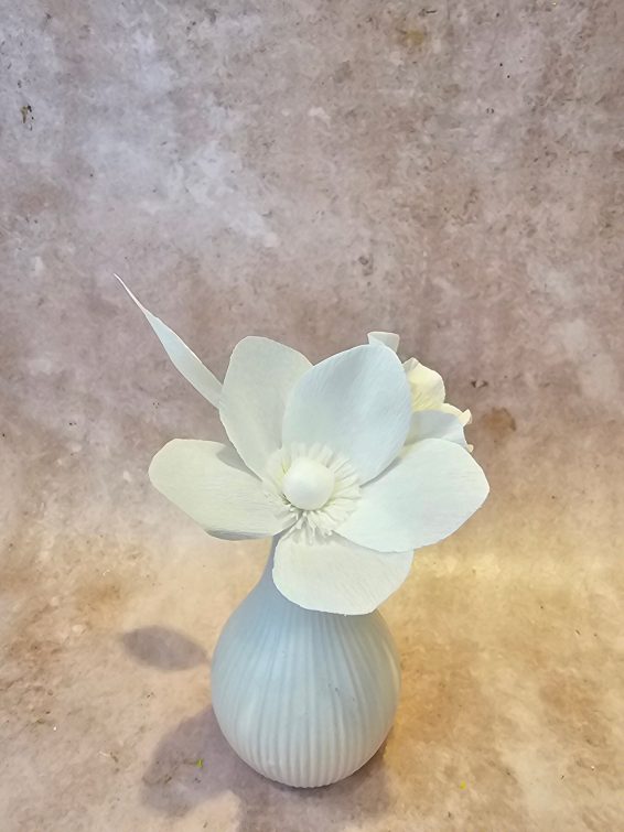 Een witte papieren bloem in een lichtblauw knopvaasje.